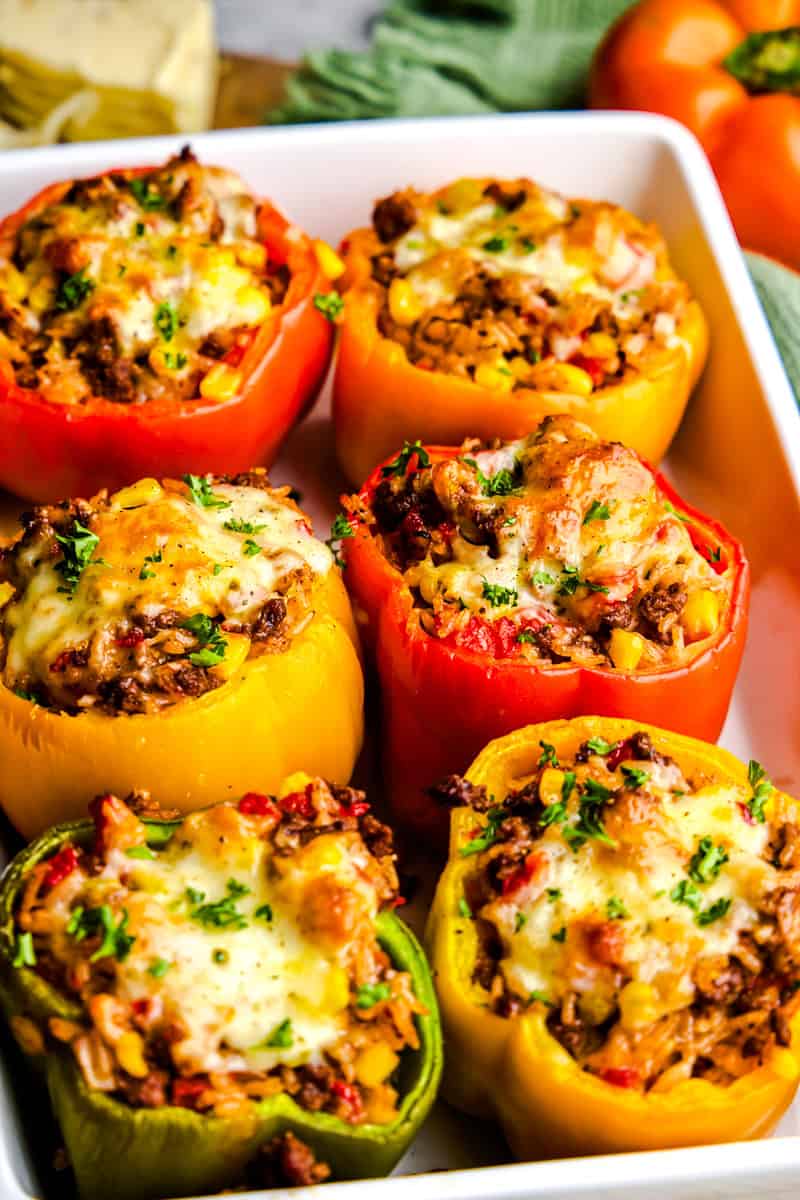 A baking dish full of simple stuffed bell pepper that is at the top with molten cheese.