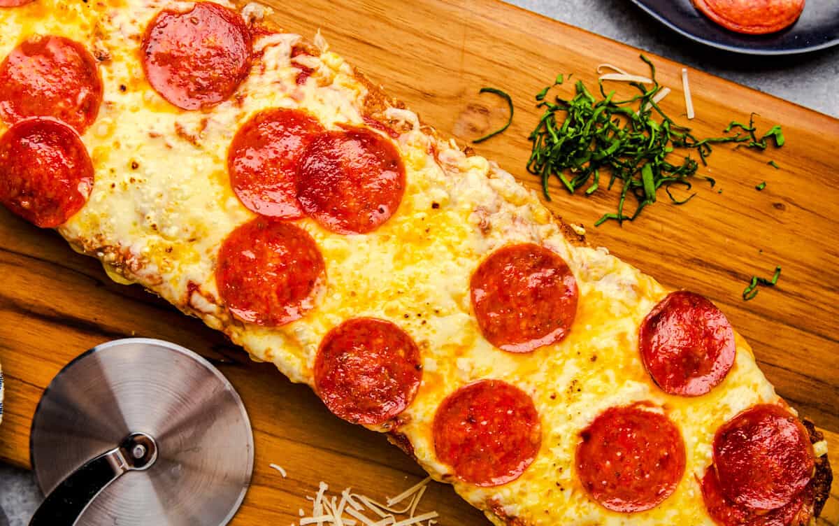 Overhead image of French Bread Pizza on a cutting board with pepperonis, cheese and basil.