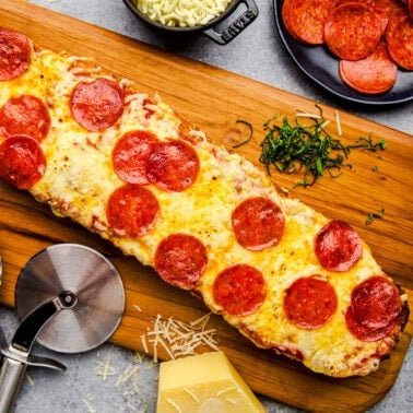 Overhead image of French Bread Pizza on a cutting board with pepperonis, cheese and basil.