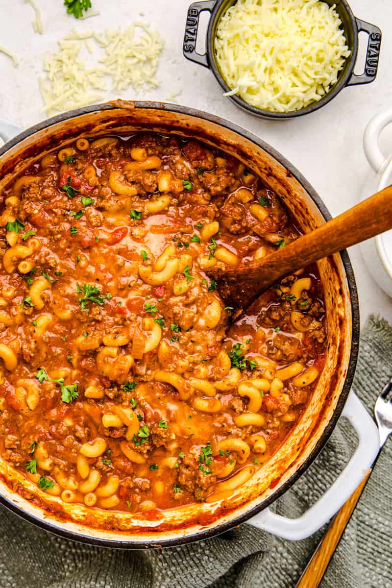 Old Fashioned American Goulash in a large pot with fresh parsley and sprinkled cheese.