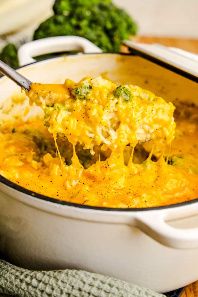 A ladle full of cheesy One Pot Chicken Broccoli & Rice in a white cast iron pot.