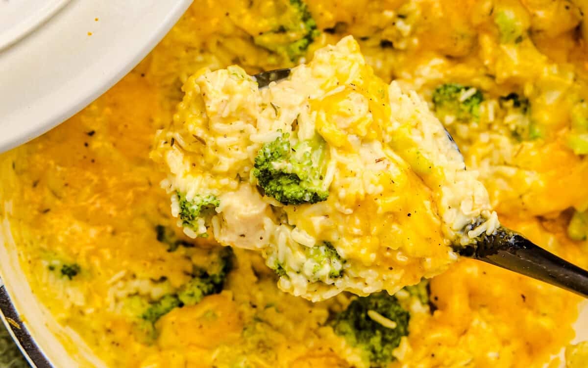 An overhead image of A ladle full of One Pot Chicken Broccoli & Rice above a white cast iron pot.