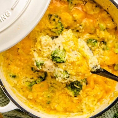 An overhead image of A ladle full of One Pot Chicken Broccoli & Rice above a white cast iron pot.