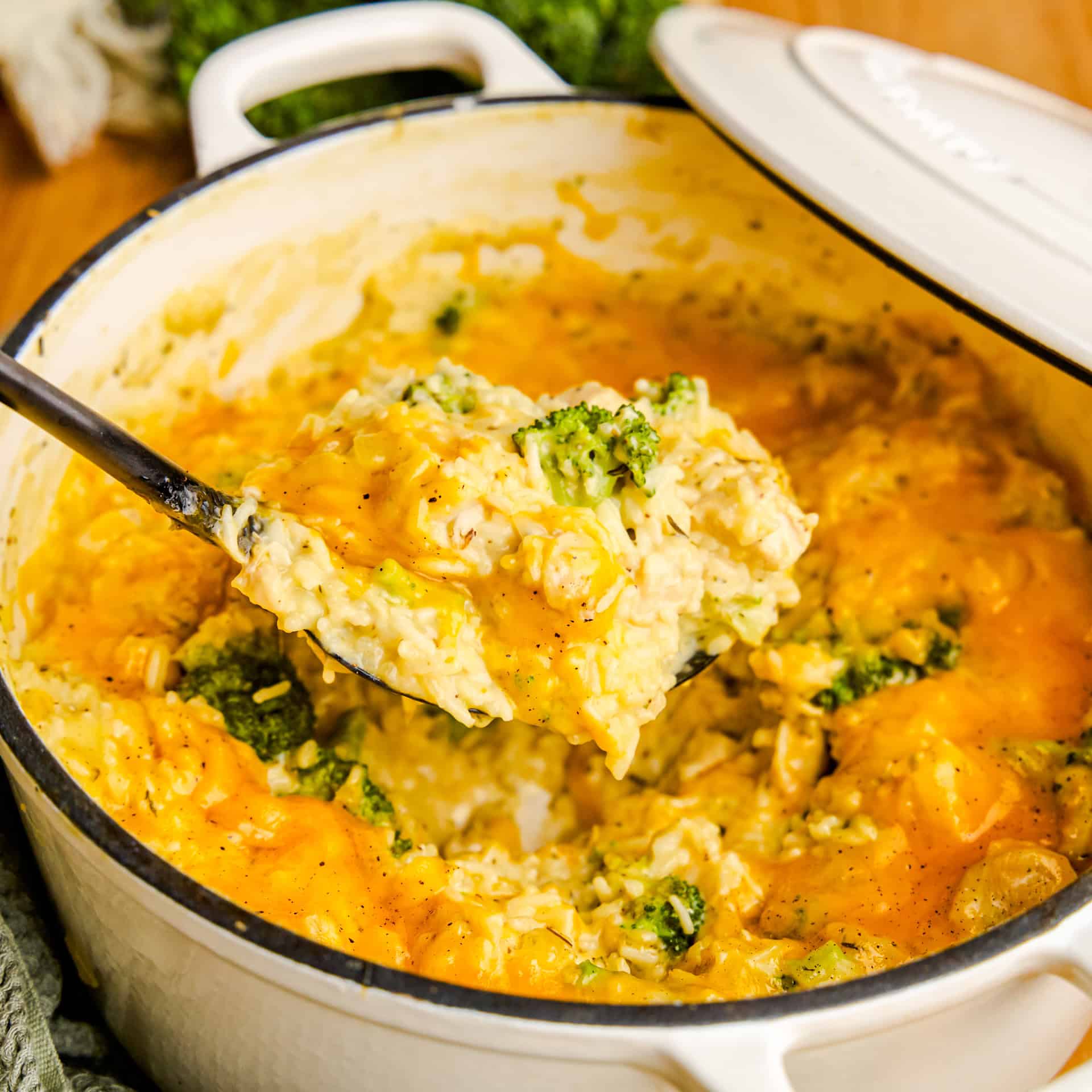 A ladle full of One Pot Chicken Broccoli & Rice in a white cast iron pot.