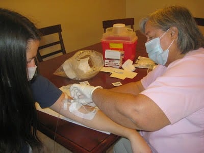 Receiving a PICC line change from a home health nurse while sitting at a kitchen table.