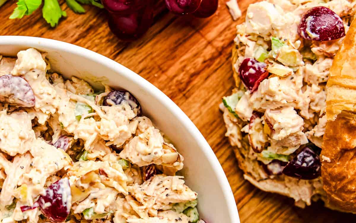 Traditional Chicken Salad in a bowl next to croissants and red grapes.