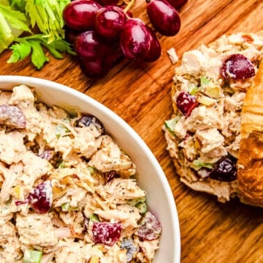 Traditional Chicken Salad in a bowl next to croissants and red grapes.