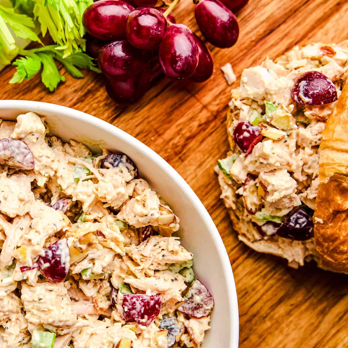 Traditional Chicken Salad in a bowl next to croissants and red grapes.