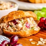 Traditional Chicken Salad sandwich in a croissant on a cutting board with grapes and almonds.