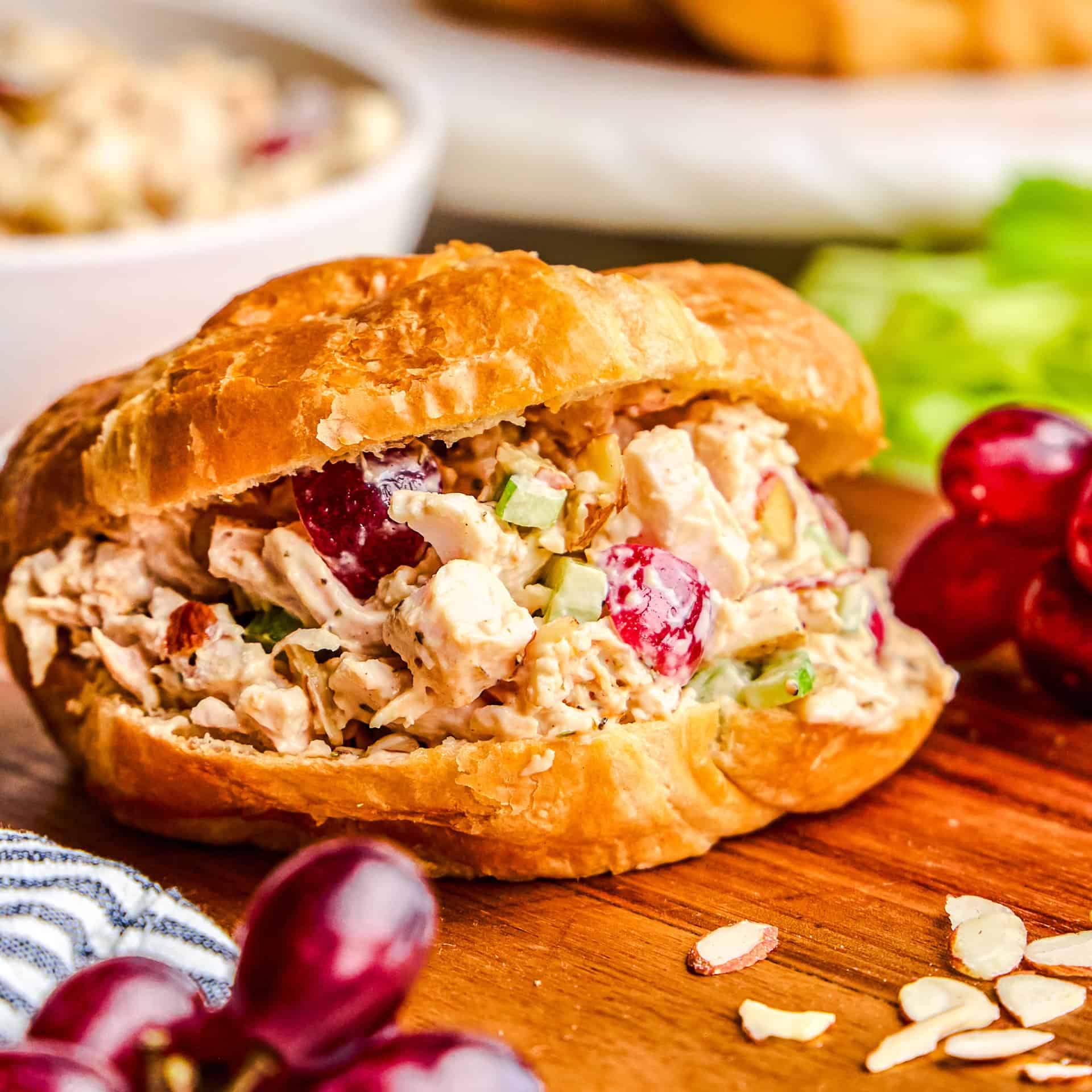 Traditional Chicken Salad sandwich in a croissant on a cutting board with grapes and almonds.