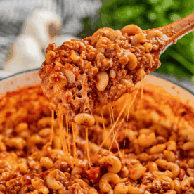 Wooden spoon filled with goulash being held over a stockpot.