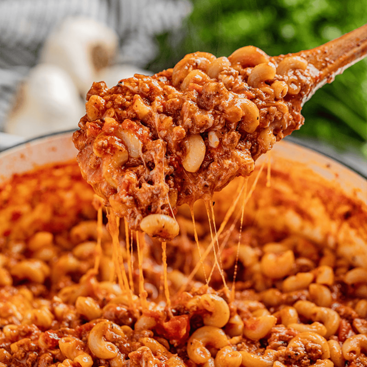Wooden spoon filled with goulash being held over a stockpot.
