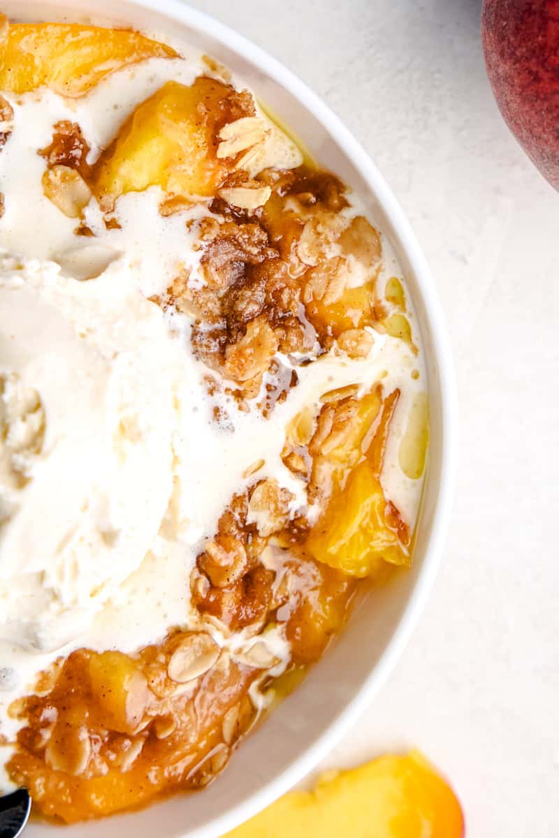 A bowl full of the Best Ever Peach Crisp with a scoop of ice cream melting on top.
