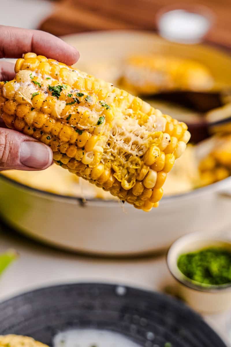 A hand holding Butter Boiled Corn on the Cob.