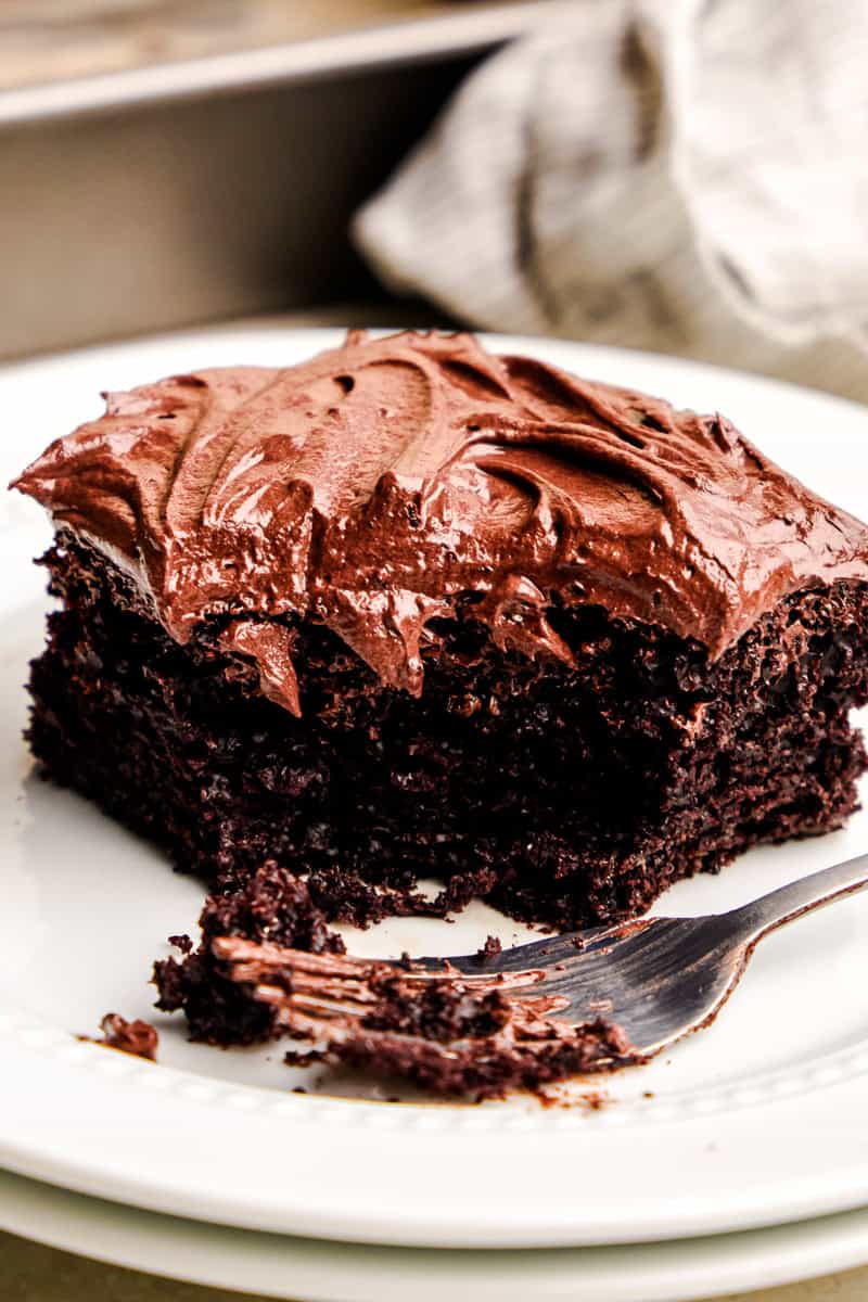 A slice of Easy Chocolate Cake on a plate with a fork and a bite taken out of it.