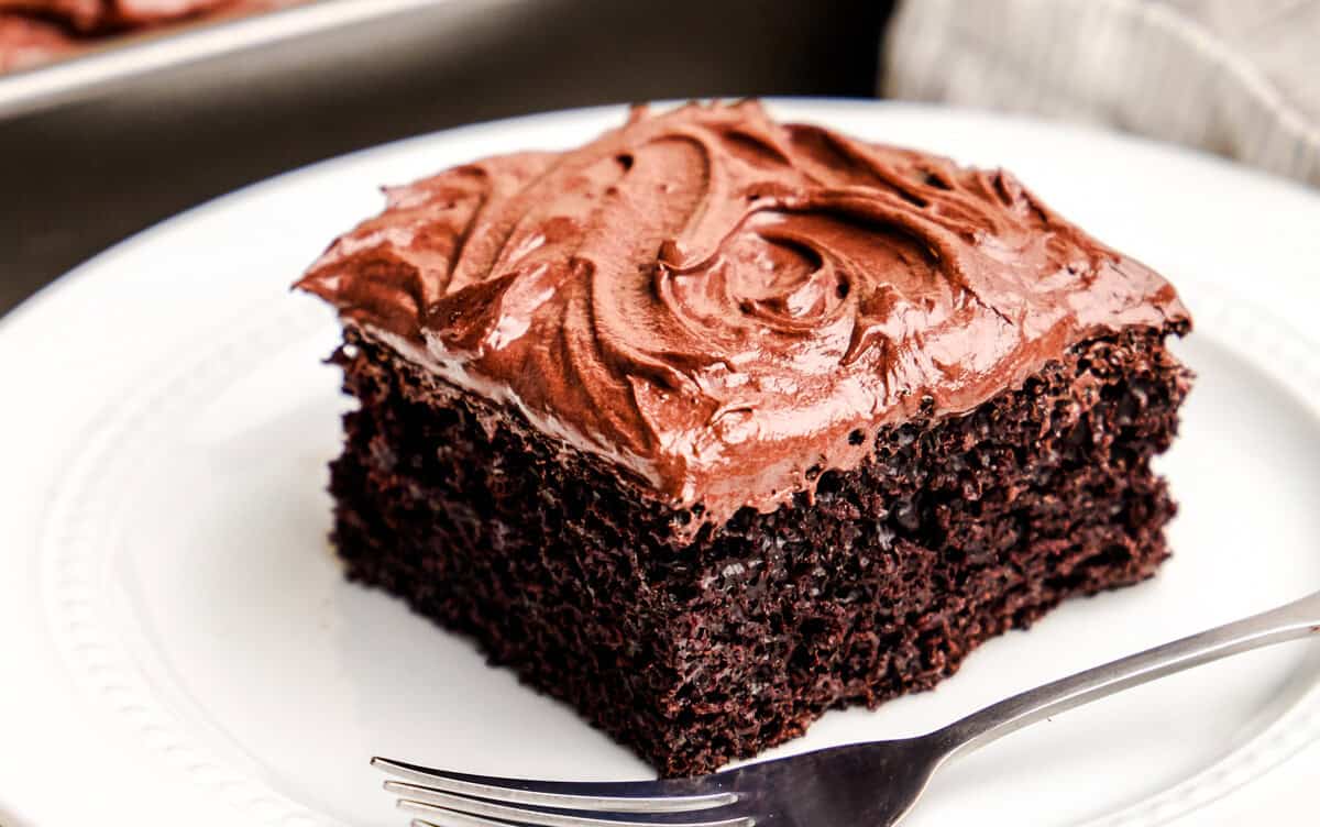A closeup image of a slice of Easy Chocolate Cake on a white plate with the cake pan in the background.
