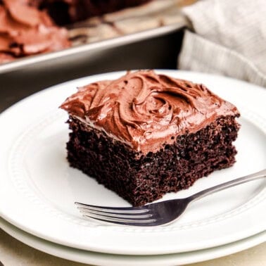 A closeup image of a slice of Easy Chocolate Cake on a white plate with the cake pan in the background.
