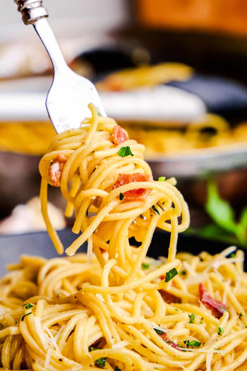 A twirled forkful of Eggless Spaghetti Carbonara hovering above a bowl.
