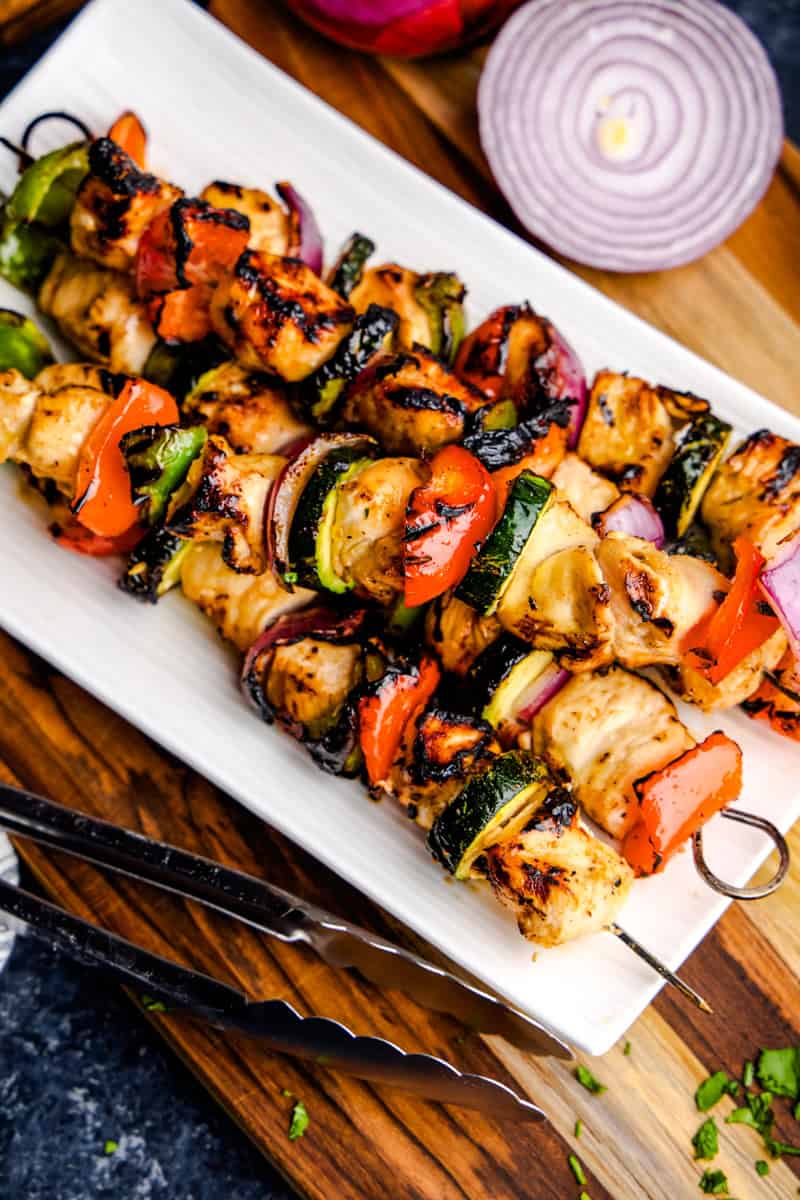 Juicy Marinated Grilled Chicken Kabobs on a white plate with tongs.