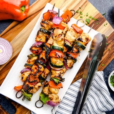 Juicy Marinated Grilled Chicken Kabobs on a white plate with tongs.