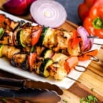 Tongs placing a Juicy Marinated Grilled Chicken Kabob on a white plate.