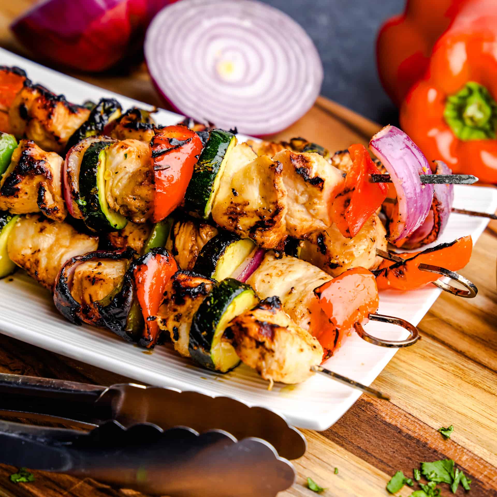Tongs placing a Juicy Marinated Grilled Chicken Kabob on a white plate.