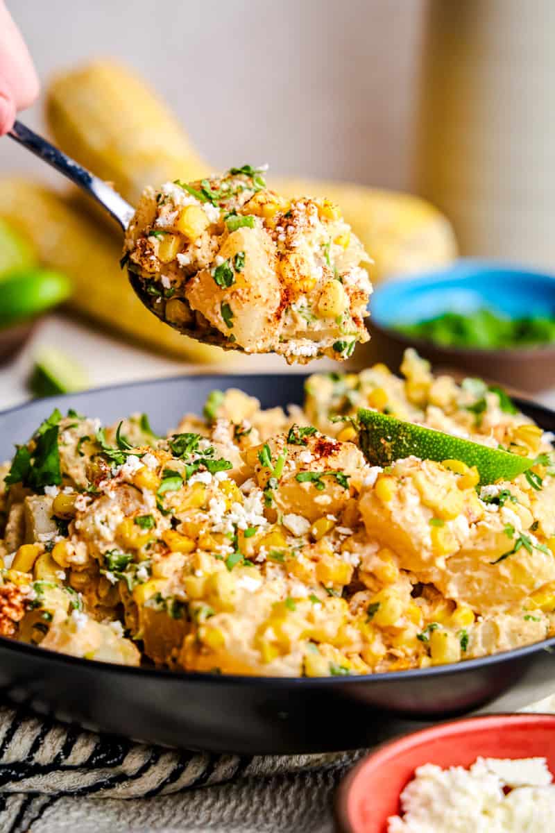 A spoon full of Mexican Street Corn Potato Salad hovering above a bowl full of salad.