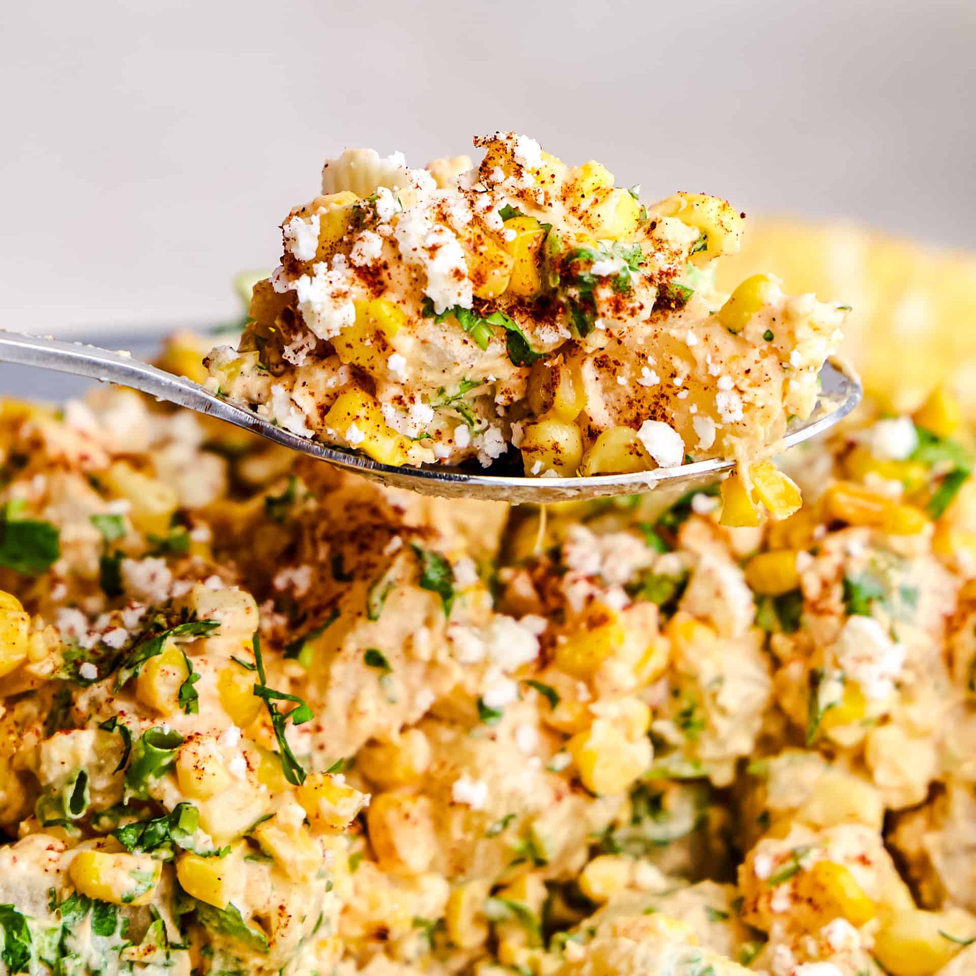 A spoon full of Mexican Street Corn Potato Salad hovering above a bowl full of salad.