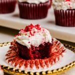 A close up image of a Most Amazing Red Velvet Cupcake topped with fluffy white frosting with a bite out of it.
