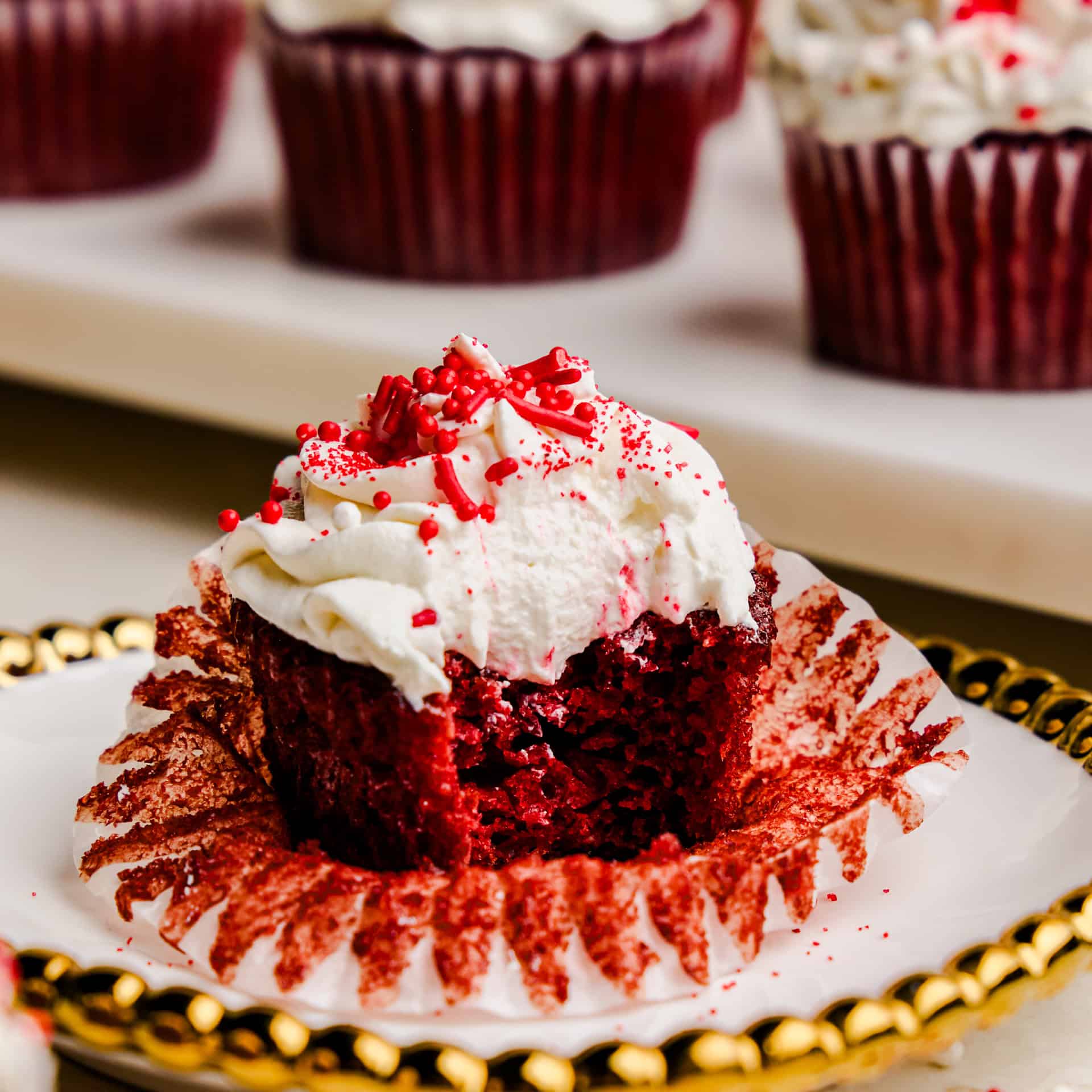 A close up image of a Most Amazing Red Velvet Cupcake topped with fluffy white frosting with a bite out of it.