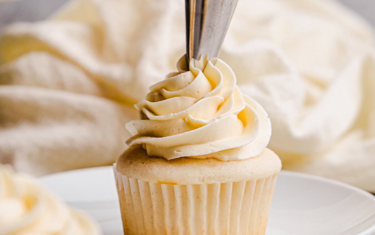 A most Amazing White Cupcake on a plate being decorated with creamy white frosting.