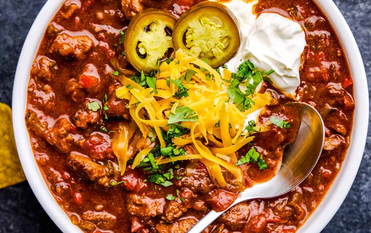 A bowl full of No Bean Chili with cheese, cilantro, yogurt and jalapeños on top.