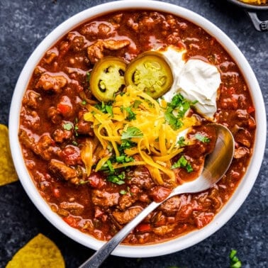 A bowl full of No Bean Chili with cheese, cilantro, yogurt and jalapeños on top.