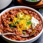 A bowl full of No Bean Chili with cheese, cilantro, yogurt and jalapeños on top.