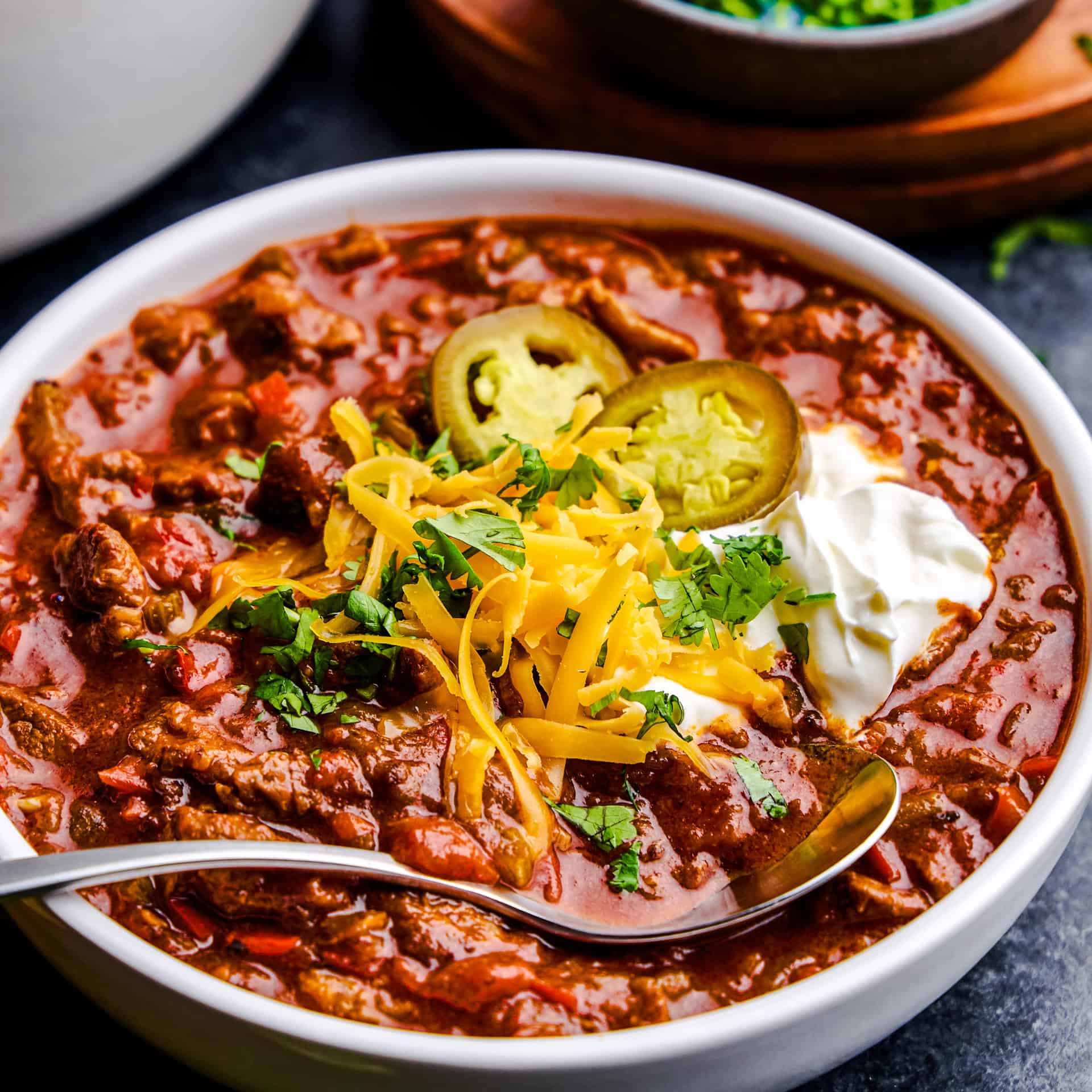 A bowl full of No Bean Chili with cheese, cilantro, yogurt and jalapeños on top.