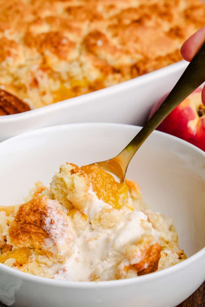 A spoon in a bowl of Old Fashioned Peach Cobbler and melty ice cream.
