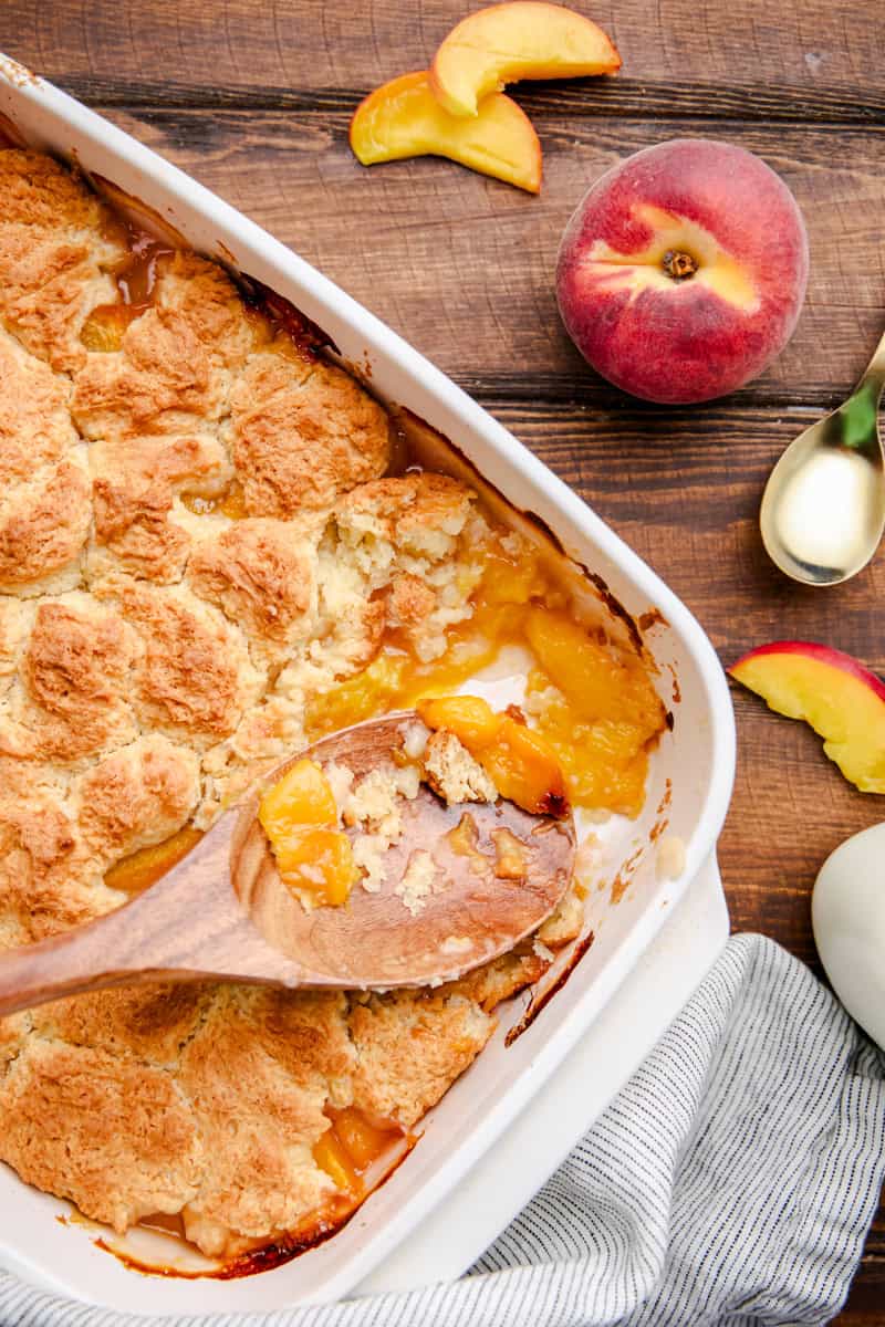 A dish of Old Fashioned Peach Cobbler with a wooden spoon in it.