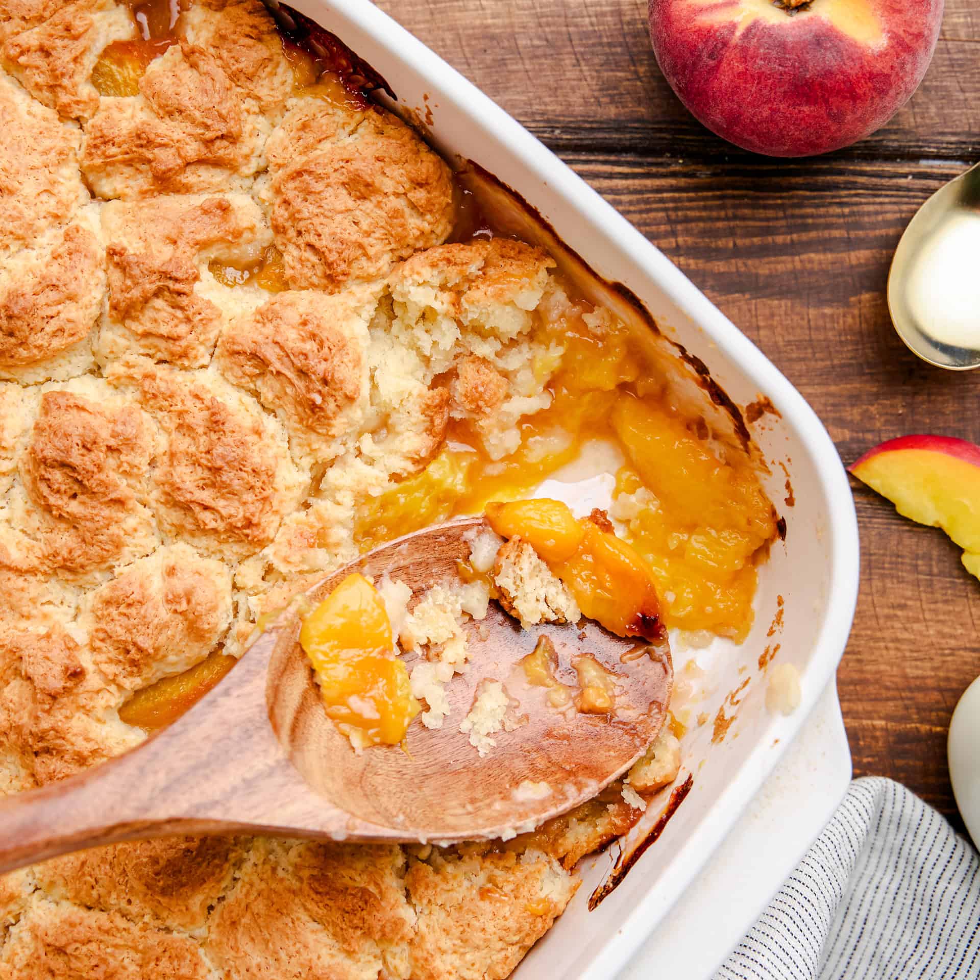 A dish of Old Fashioned Peach Cobbler with a wooden spoon in it.
