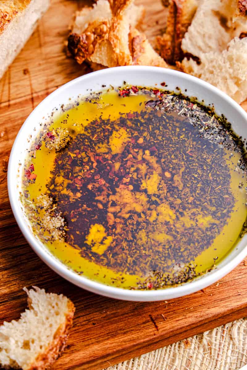 Olive Oil Bread Dip on a cutting board with fresh bread pieces around.