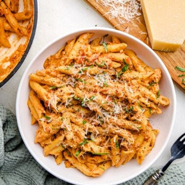 An overhead image Penne Alla Vodka in a bowl topped with parmesan and basil.
