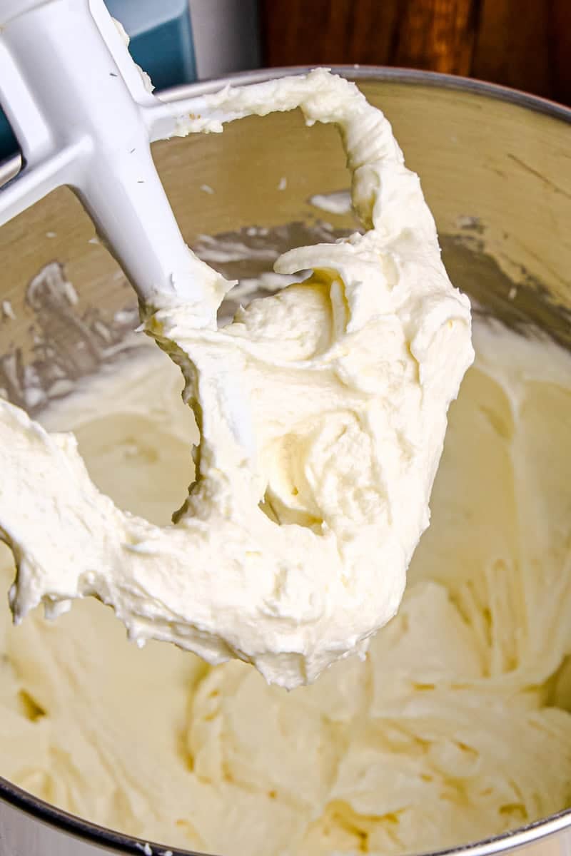 A mixer whisk and bowl with creamy Perfect Cream Cheese Frosting in and on them.