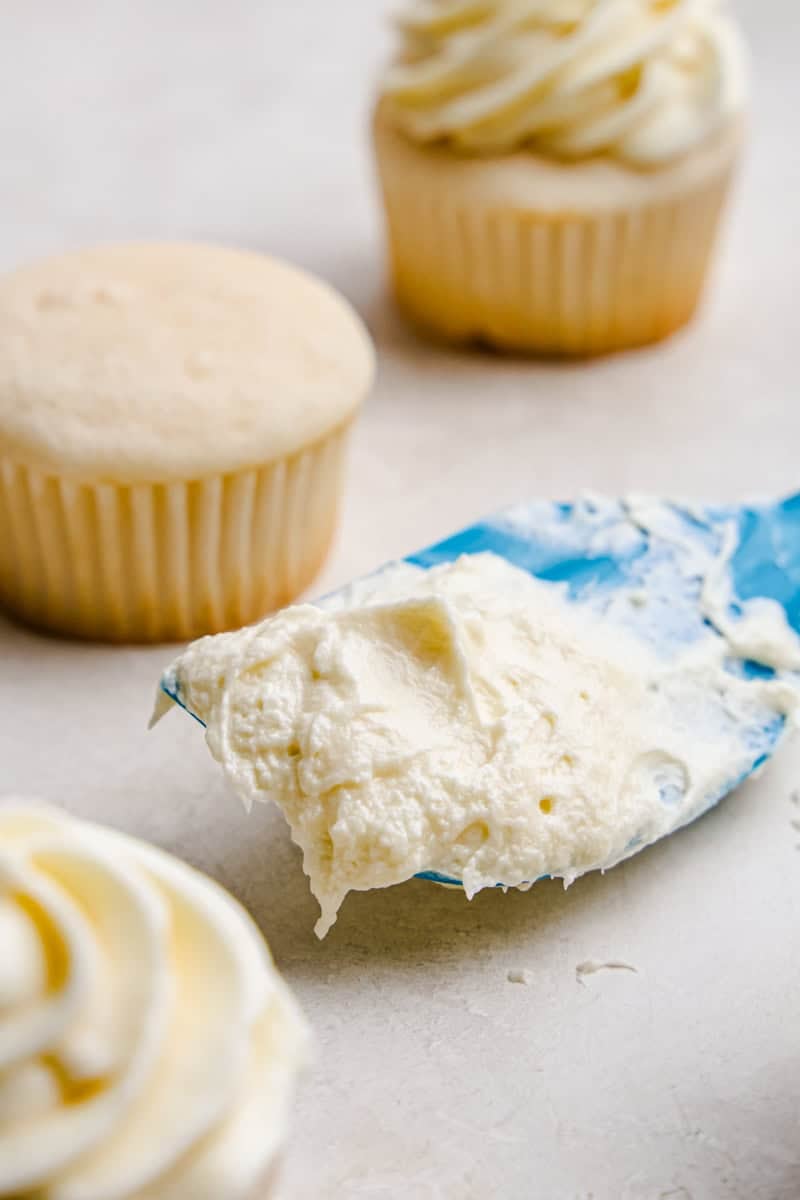A spatula with Perfect Cream Cheese Frosting on it and a few cupcakes sitting near.