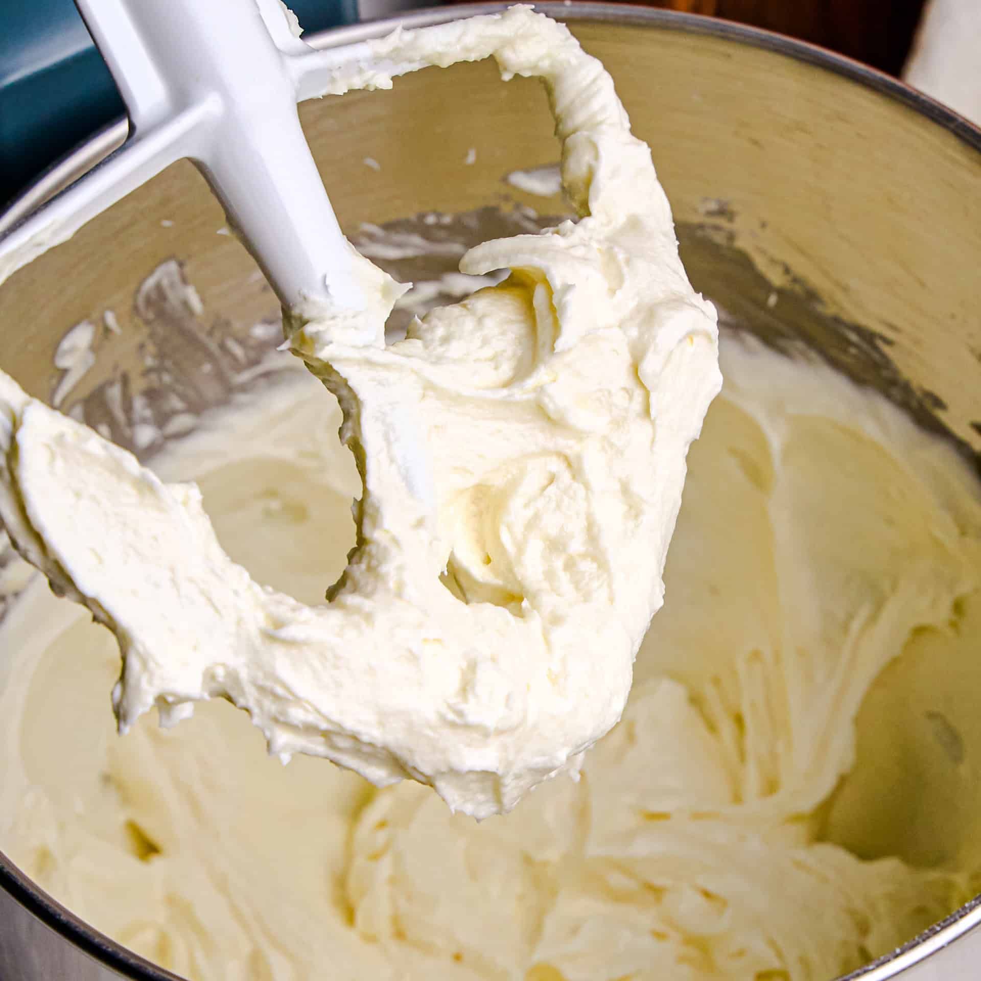 A mixer whisk and bowl with creamy Perfect Cream Cheese Frosting in and on them.