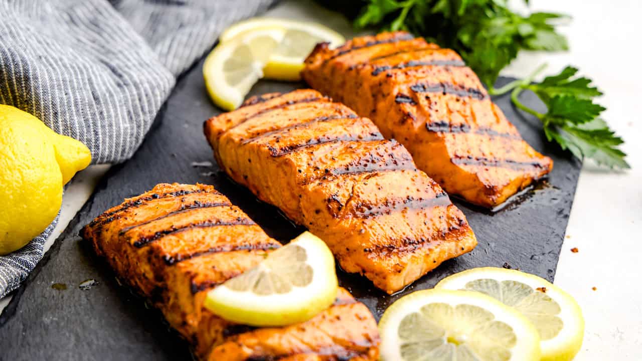 Three Simple Grilled Salmon filets on a black slate serving platter with lemons.