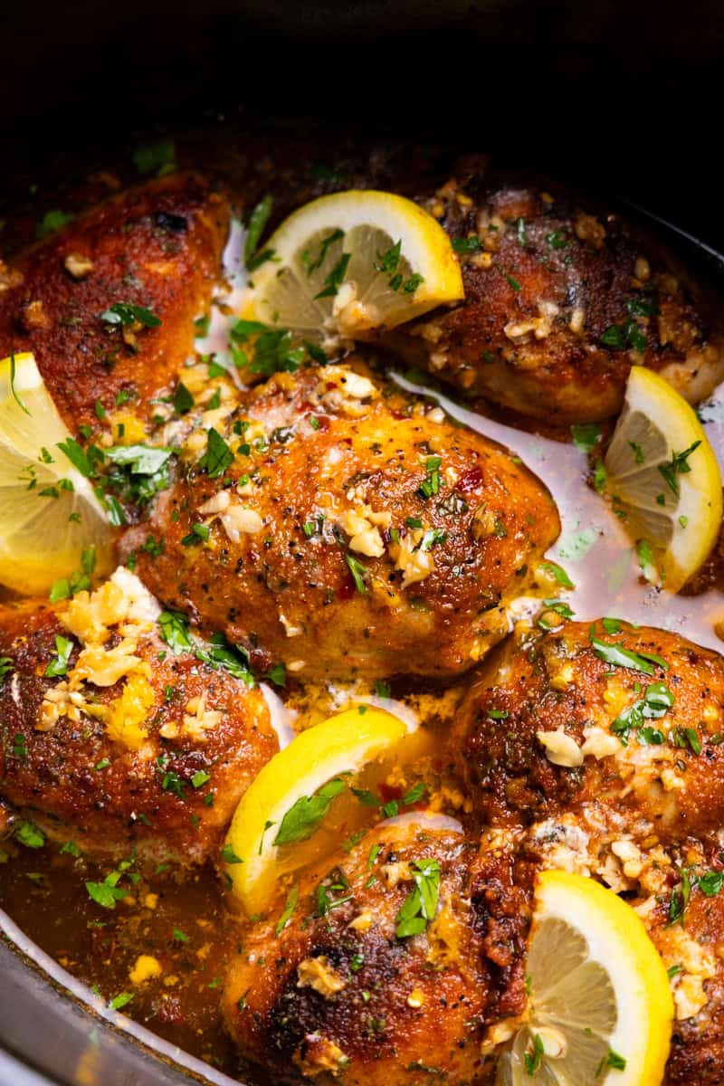 A closeup view of chicken thighs swimming in a buttery lemon garlic sauce and garnished with lemon slices.
