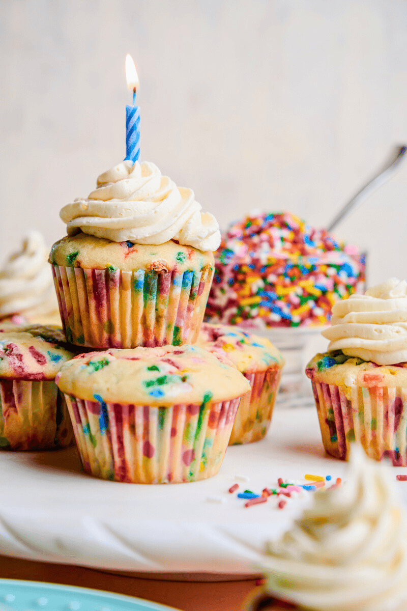 A Funfetti Birthday Cupcake with frosting and a candle stacked on top of more cupcakes.