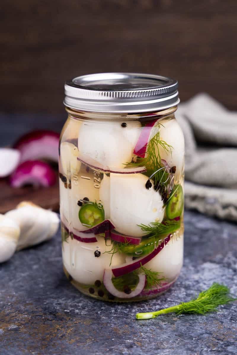 A jar of homemade pickled eggs with red onion, black peppercorns, fresh dill, and jalapeno.