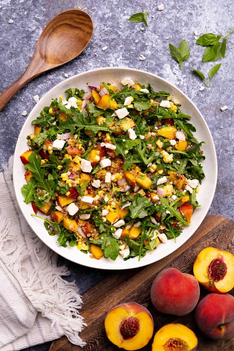 An overhead view of a bowl of peach farro salad with fresh corn, arugula, feta cheese, and red onion.