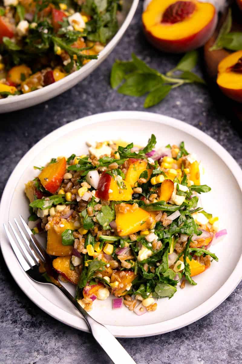A plate of peach farro salad with arugula, feta, and fresh corn. There's a fork resting on the plate.