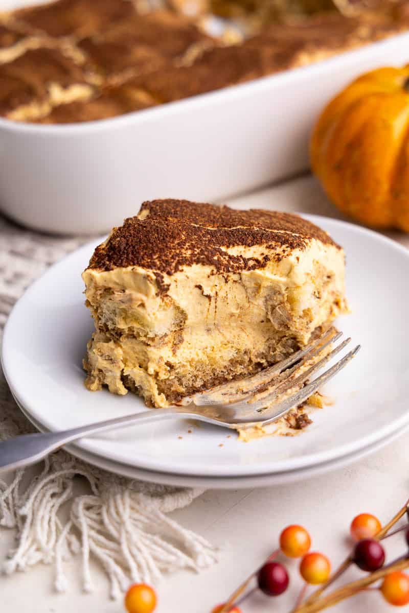 A piece of pumpkin spice tiramisu on a white plate. A bite has been taken out and the fork is resting on the plate.